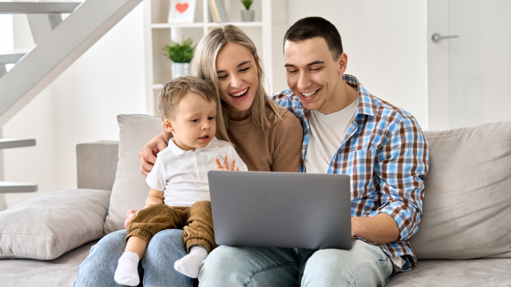 mom, dad, and child sit on couch with laptop on lap open.