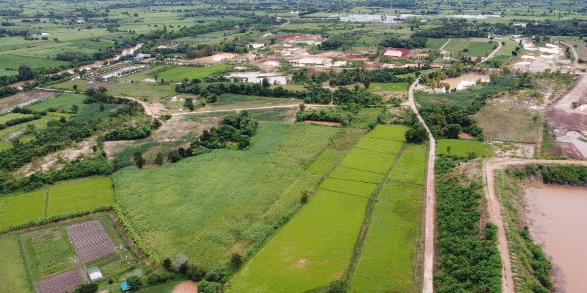 An aerial shot of a vast rural landscape with green fields and small patches of water. The area is divided by dirt roads and surrounded by various farmlands, emphasizing the rural setting's connectivity challenges. Keywords: how to get internet in rural areas.