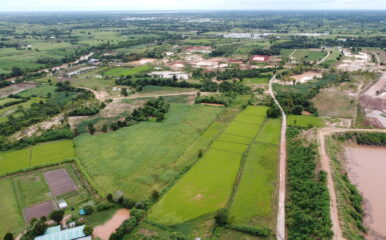 An aerial shot of a vast rural landscape with green fields and small patches of water. The area is divided by dirt roads and surrounded by various farmlands, emphasizing the rural setting's connectivity challenges. Keywords: how to get internet in rural areas.