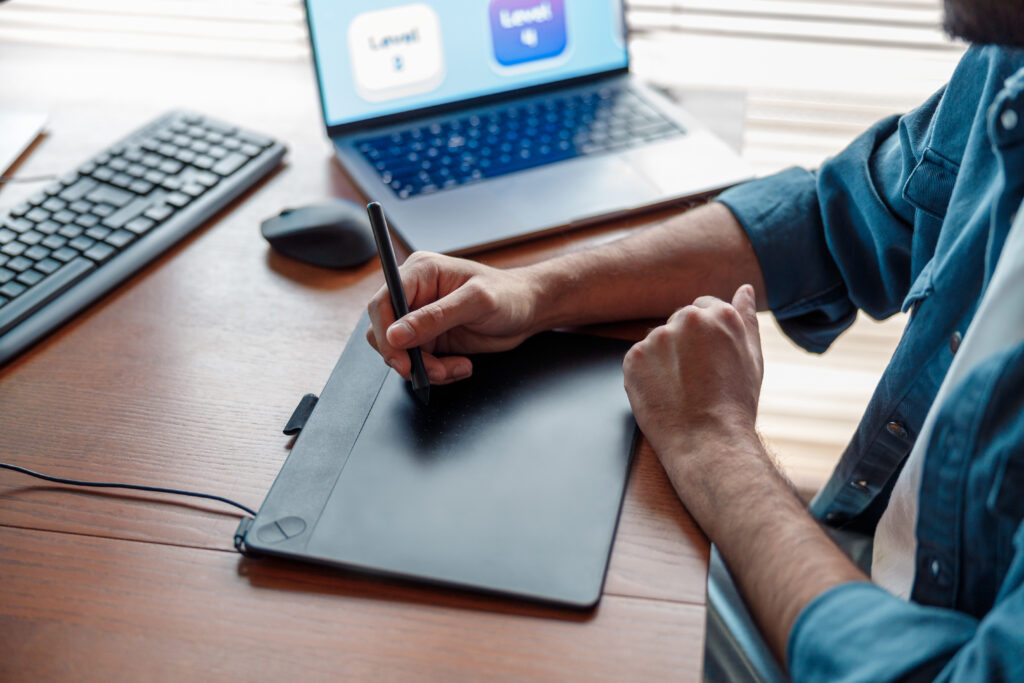 A person using a digital drawing tablet while working on a laptop in a home office, showcasing creative freedom and connectivity, essential aspects supported by the "Internet Essentials application."