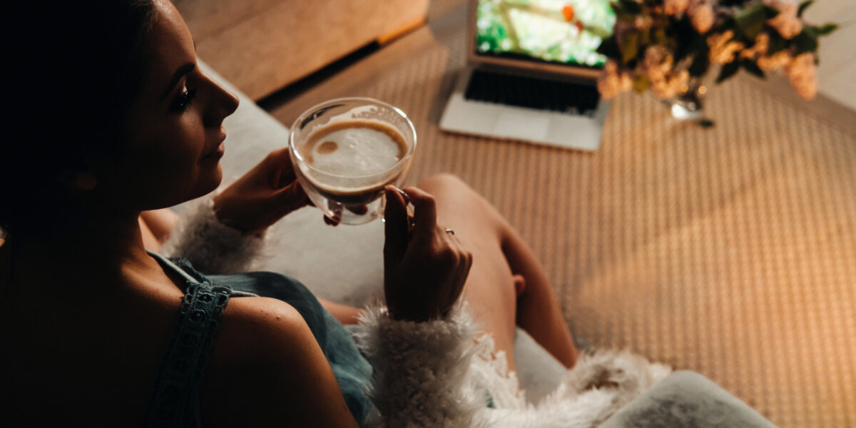 A woman enjoying a cup of coffee while watching a movie on her laptop, contemplating the benefits of Roku TV vs Google TV for a more immersive viewing experience.