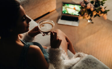 A woman enjoying a cup of coffee while watching a movie on her laptop, contemplating the benefits of Roku TV vs Google TV for a more immersive viewing experience.