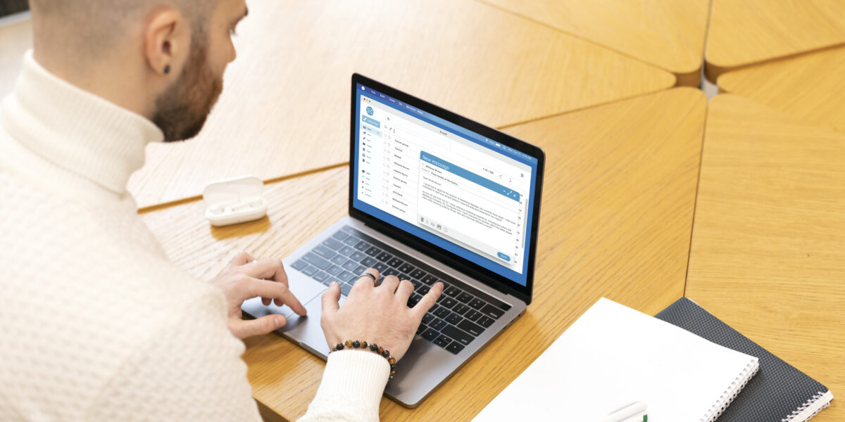 A young man in a white sweater typing on a laptop in a bright, modern study environment, reflecting a focused approach to completing tasks related to the "Internet Essentials application.