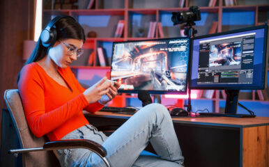 a young woman, likely a game streamer, focused on her smartphone while sitting at a desk with a high-tech setup, including dual monitors displaying a video game stream. This scene could represent the challenge of balancing multiple platforms while addressing a "cancel directv" related to content streaming.