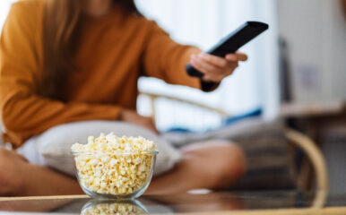 Close-up of a woman reaching for popcorn with the remote in hand, eagerly selecting from the best movies to stream today.