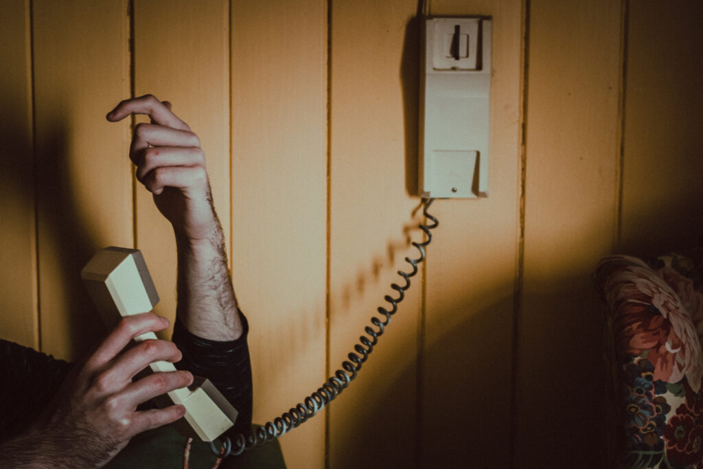 A hand holding a beige basic phone handset connected to a wall, capturing a nostalgic, vintage feel with a warm-toned background.