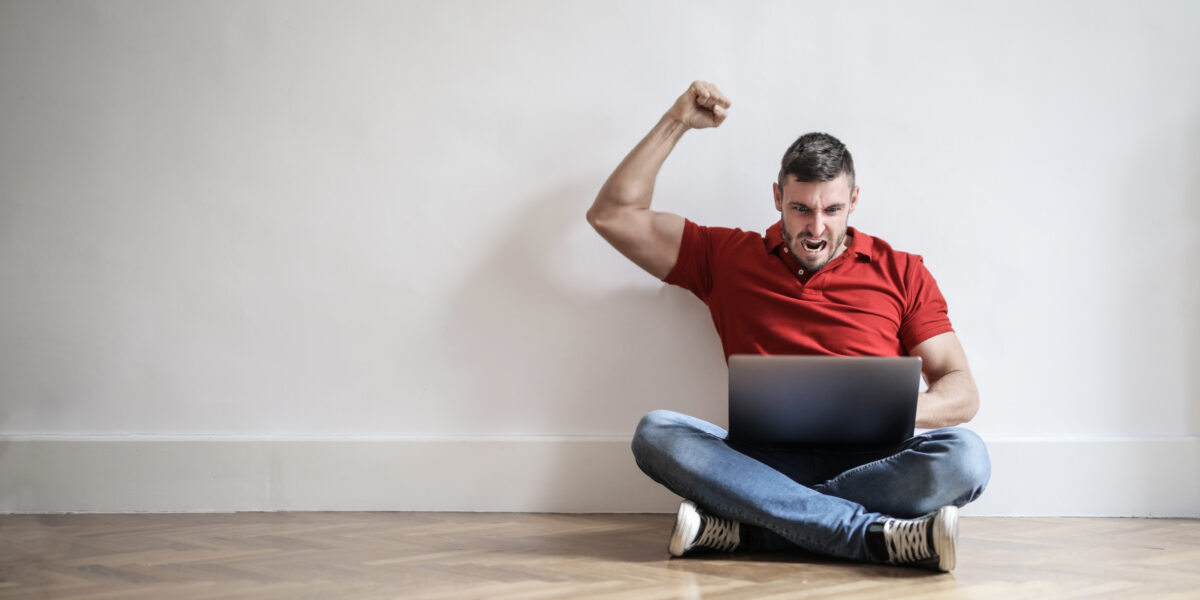 A cheerful man celebrates a successful internet connection while sitting on the floor with his laptop, symbolizing excitement after using a test my speed service to confirm fast performance.