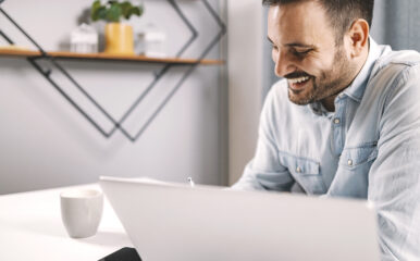 A smiling entrepreneur working in a cozy home office, engaged with his laptop while sipping coffee, showcasing a relaxed setup perfect for checking internet speed. Keywords: test my internet speed.