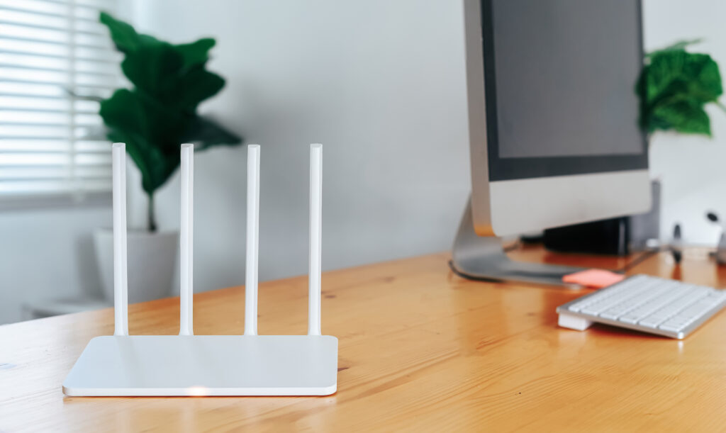 A sleek white Wi-Fi router with multiple antennas positioned on a wooden desk in a modern home office, next to a desktop computer, ideal for testing internet speed performance. Keywords: "test my internet speed."