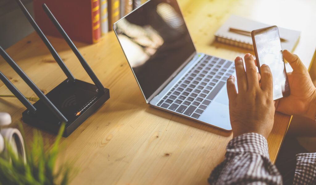 Close-up of a hand holding a smartphone near a laptop and a router, with an emphasis on "What Does MBPS Mean for Internet?"—highlighting the importance of internet speed on mobile connectivity.