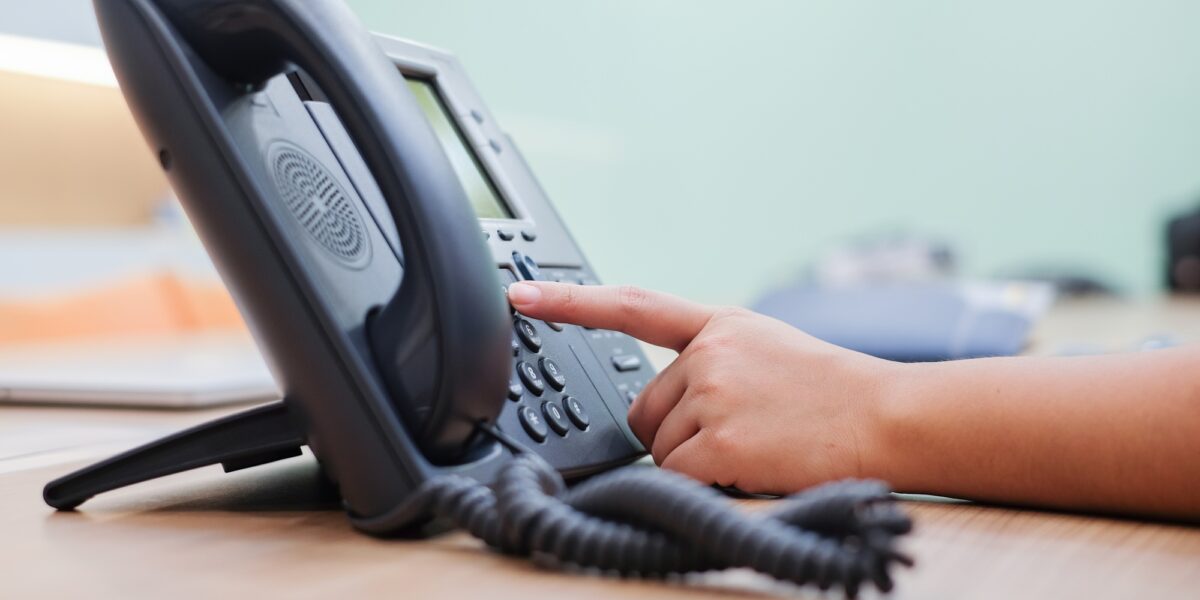 A close-up of a person’s hand dialing a number on a landline phone at an office desk, showcasing the importance of the best landline phone service for seamless and consistent connectivity in professional settings.