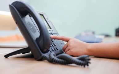 A close-up of a person’s hand dialing a number on a landline phone at an office desk, showcasing the importance of the best landline phone service for seamless and consistent connectivity in professional settings.