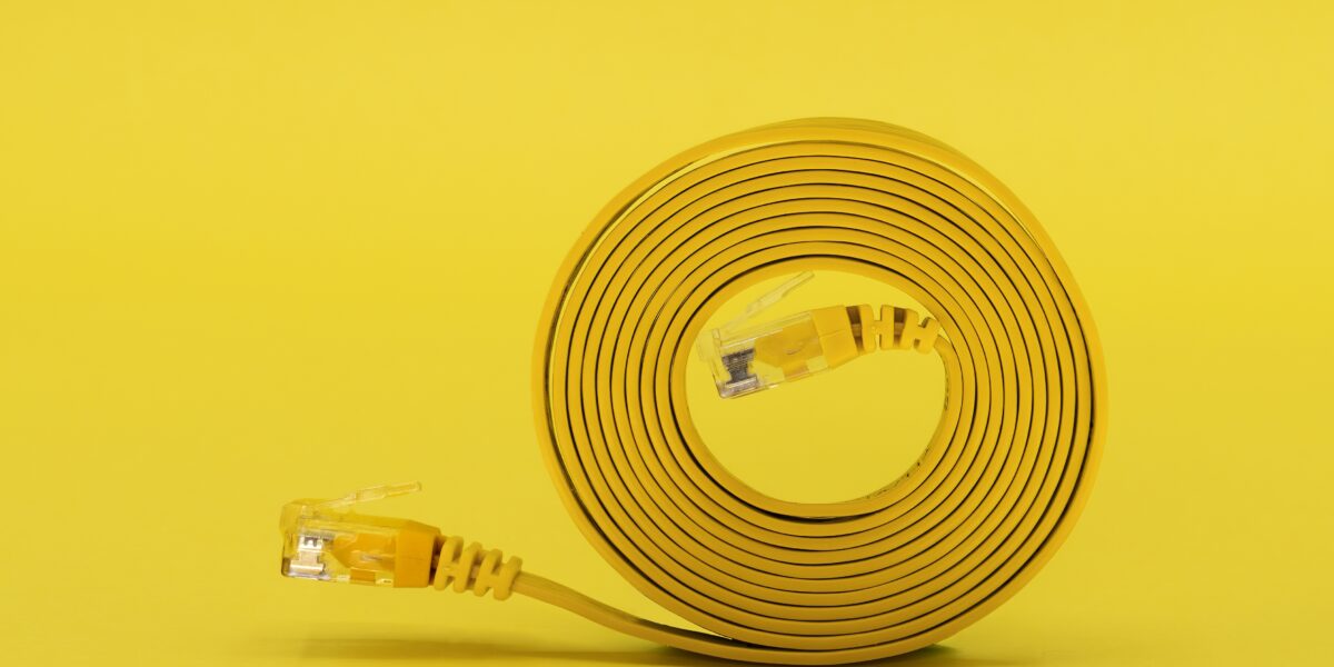 A neatly coiled yellow network cable with visible connectors sits against a bold yellow background, representing efficient and streamlined solutions for the best internet speedtest performance.