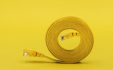 A neatly coiled yellow network cable with visible connectors sits against a bold yellow background, representing efficient and streamlined solutions for the best internet speedtest performance.