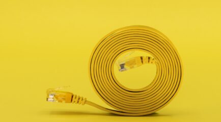 A neatly coiled yellow network cable with visible connectors sits against a bold yellow background, representing efficient and streamlined solutions for the best internet speedtest performance.