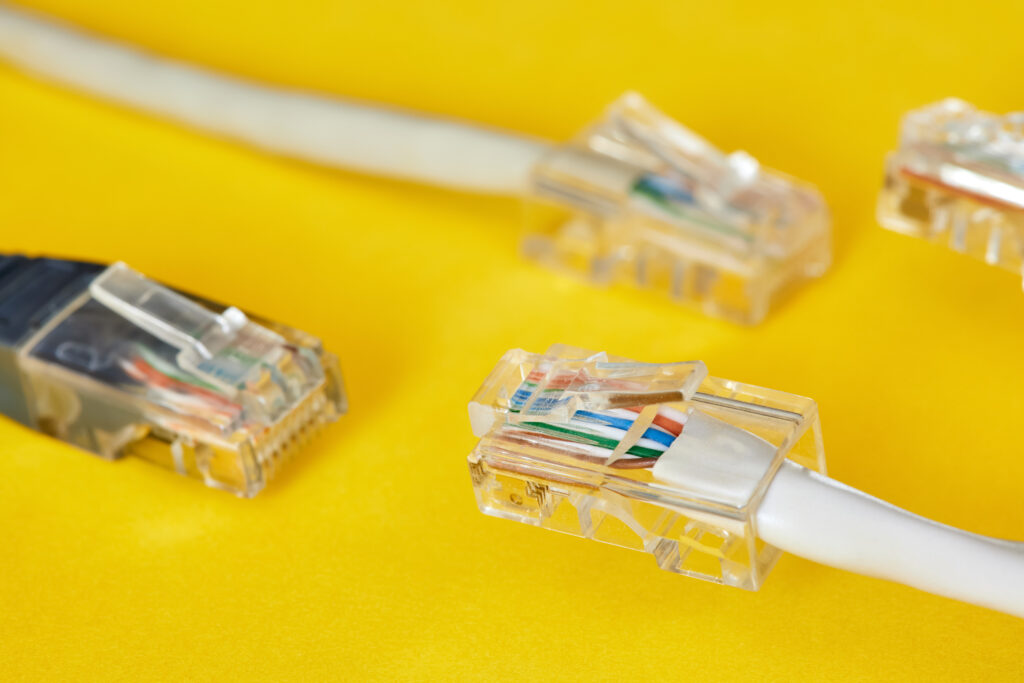 A close-up view of various Ethernet cables and RJ45 connectors on a yellow background, showcasing the essential tools for delivering the best internet speedtest outcomes.