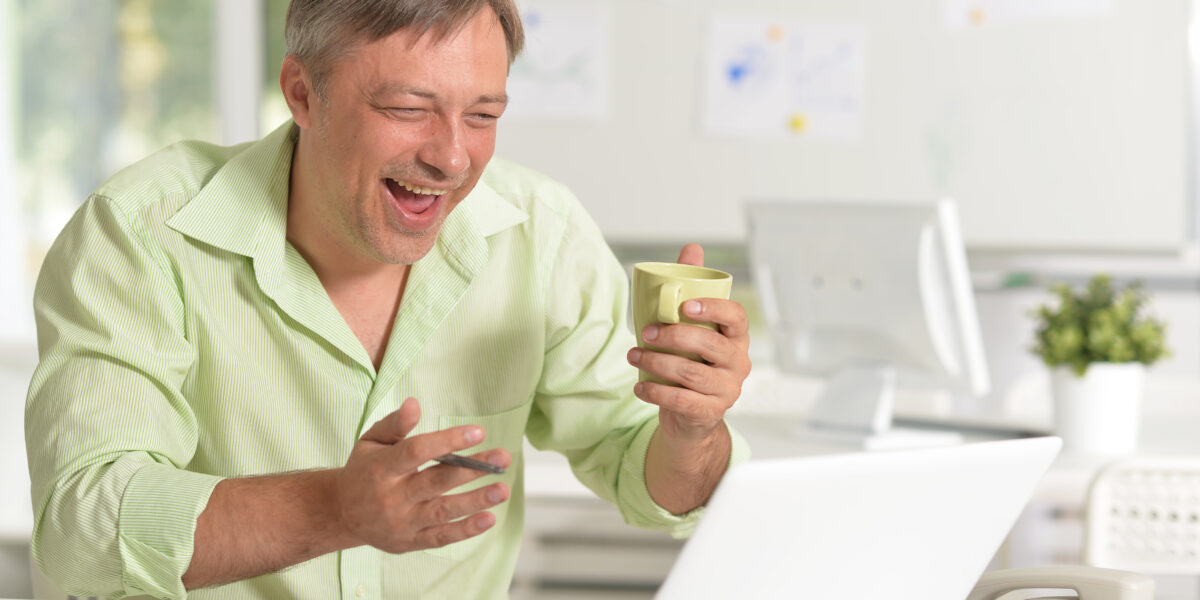 A smiling man enjoys a video call or online activity while holding a coffee cup, thanks to the best cable internet deals that deliver fast and reliable connectivity for work and leisure.