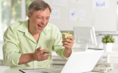 A smiling man enjoys a video call or online activity while holding a coffee cup, thanks to the best cable internet deals that deliver fast and reliable connectivity for work and leisure.