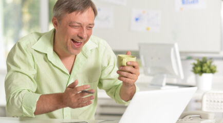 A smiling man enjoys a video call or online activity while holding a coffee cup, thanks to the best cable internet deals that deliver fast and reliable connectivity for work and leisure.