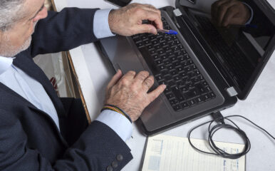 Mature man in a suit working on a laptop with a pen in hand, reflecting a professional setting where "check my computer speed" ensures optimal workflow and responsiveness.