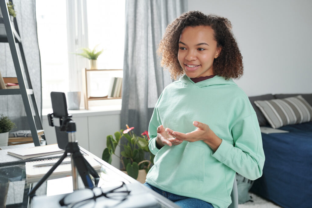 A teenage girl sits in her bedroom, recording a video on her smartphone for an online seminar. This scene highlights how the best internet for apartment living enables seamless content creation and online learning.