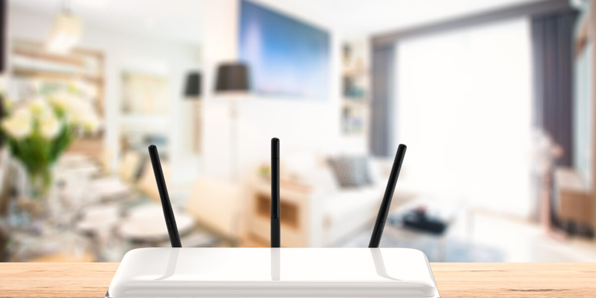 A sleek white WiFi router with three antennas is positioned on a wooden table in a brightly lit, modern living room. This image highlights the ideal central placement of the router for optimal connectivity in a stylish home setting. Keywords: WiFi router placement, modern home, best place to put WiFi router in house.