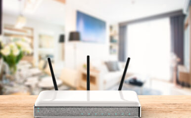 A sleek white WiFi router with three antennas is positioned on a wooden table in a brightly lit, modern living room. This image highlights the ideal central placement of the router for optimal connectivity in a stylish home setting. Keywords: WiFi router placement, modern home, best place to put WiFi router in house.