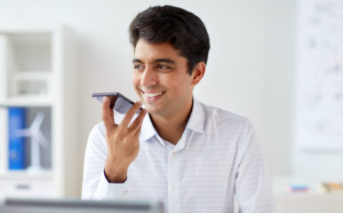 A smiling businessman using a smartphone's voice command feature in a bright office, showcasing the integration of "caller ID phone" and smart technology.