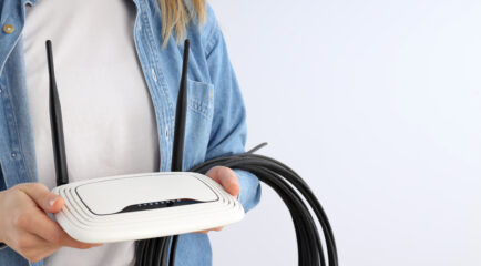 A person holding a white WiFi router with cables against a plain background, representing technical aspects and lifespan inquiries such as 