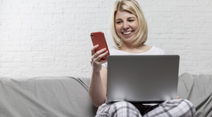 Smiling woman using her smartphone and laptop on a couch, symbolizing seamless connectivity with 