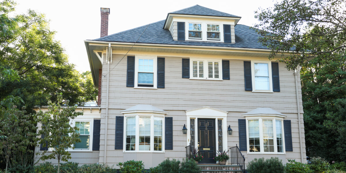 A suburban two-story house with a landscaped yard, illustrating the challenges of achieving reliable WiFi coverage throughout the home. Keywords: "best place to put wifi router in a 2 story house."