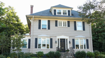 A suburban two-story house with a landscaped yard, illustrating the challenges of achieving reliable WiFi coverage throughout the home. Keywords: 