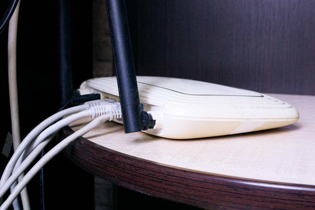 A close-up view of a slightly aged WiFi router with connected ethernet cables, placed on a wooden shelf. The image showcases a typical placement for routers in homes, though it subtly suggests that a more open location might improve signal strength. Keywords: WiFi router placement, ethernet cables, best place to put WiFi router in house.