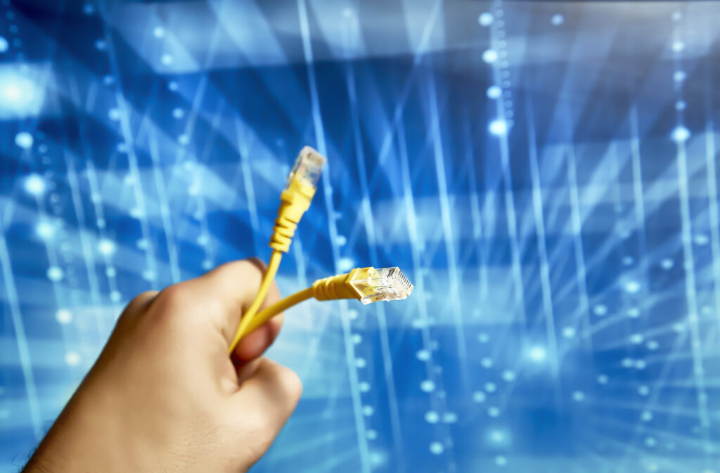 A close-up of a hand holding yellow network cables with RJ-45 connectors, set against a digital blue background representing high-speed data transmission. This visually encapsulates the essence of commercial fiber internet reliability and speed.