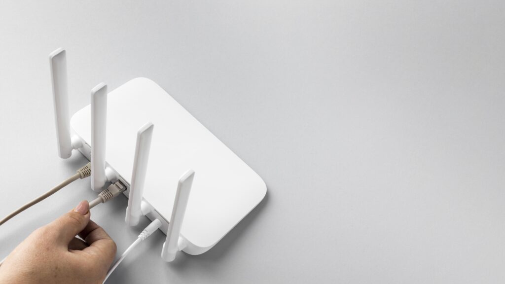 A close-up of a white WiFi router with four antennas, as a person plugs in an Ethernet cable. This setup suggests troubleshooting steps on how to fix slow WiFi by using a wired connection for better internet speed.