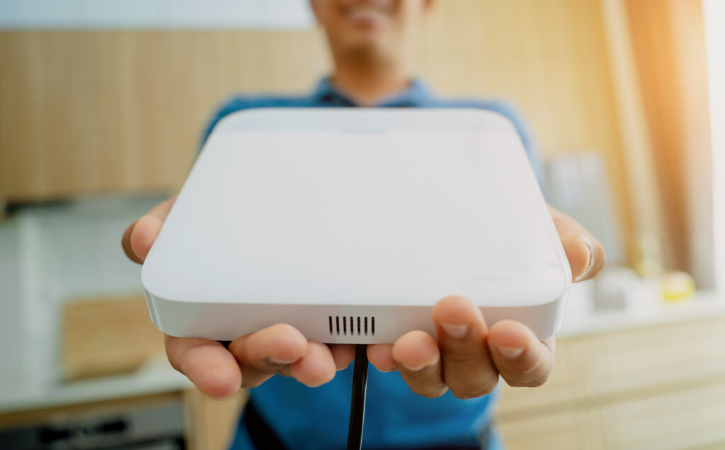 A person holding a sleek, modern internet box for home, presenting it towards the camera in a well-lit kitchen setting.