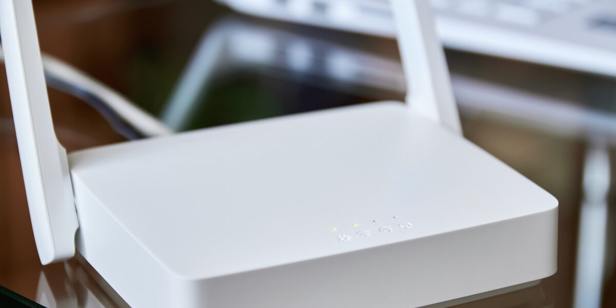 A white internet box for home with indicator lights, placed on a glass table near a laptop, ensuring seamless wireless connectivity.