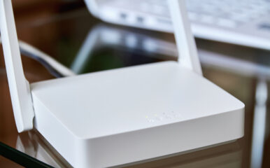 A white internet box for home with indicator lights, placed on a glass table near a laptop, ensuring seamless wireless connectivity.