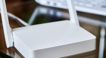 A white internet box for home with indicator lights, placed on a glass table near a laptop, ensuring seamless wireless connectivity.