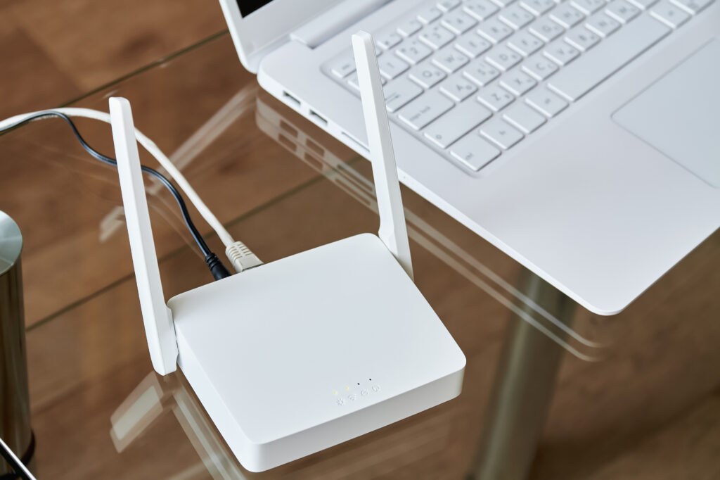 A close-up of a white internet box for home with antennas and ethernet cables connected, sitting next to a laptop on a glass desk for high-speed internet access.